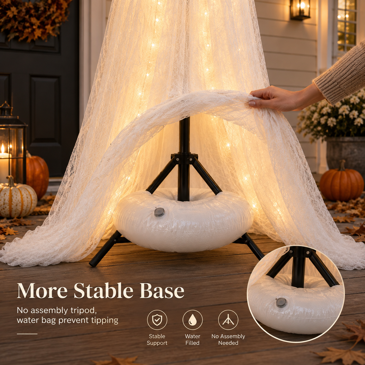 A white inflatable water-filled base with a black tripod stand supporting a draped white netting covered in warm white fairy lights, shown outdoors on a porch with pumpkins and a hand adjusting the netting. Text reads 'More Stable Base' with feature icons.